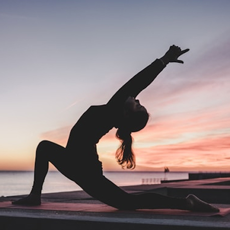 Woman practicing a yoga pose against a sunset backdrop, emphasizing relaxation, balance, and well-being.